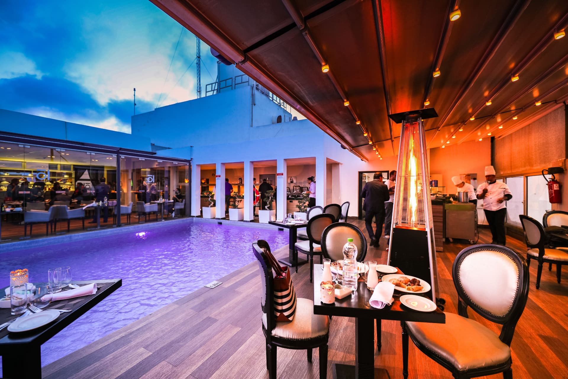 An open-air restaurant beside a swimming pool at dusk